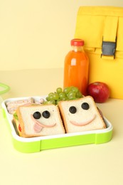 Bag, sandwiches with smiley faces in lunch box and bottle of juice a on yellow background