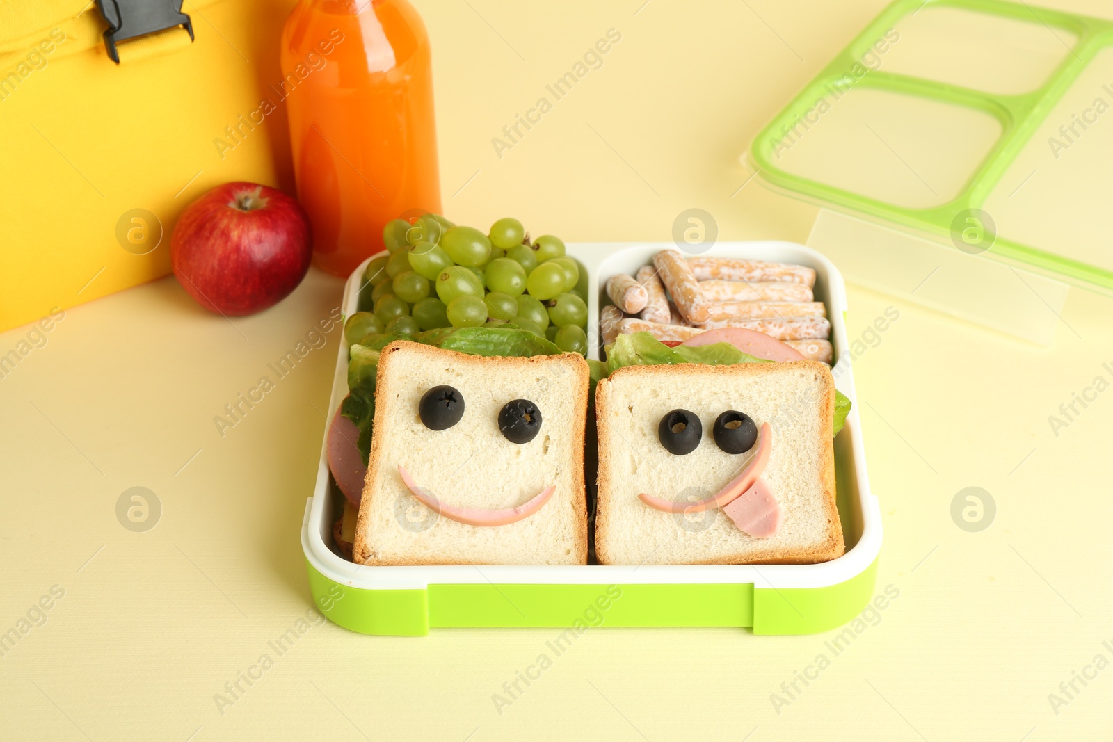 Photo of Bag, sandwiches with smiley faces in lunch box and bottle of juice a on yellow background