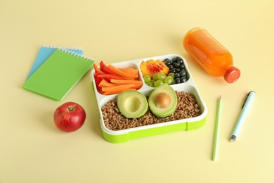 Photo of Lunch box with snacks, bottle of juice and stationery on yellow table