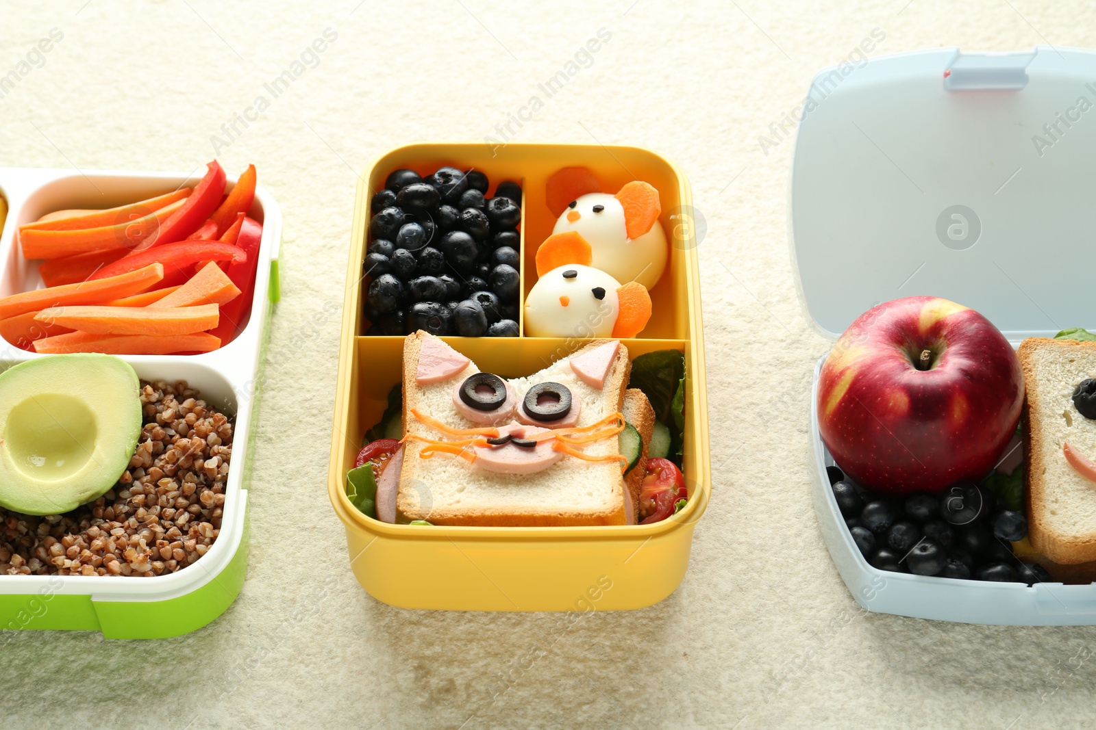 Photo of Lunch boxes with different snacks on beige textured table, closeup