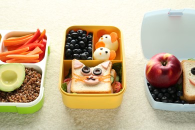 Photo of Lunch boxes with different snacks on beige textured table, closeup