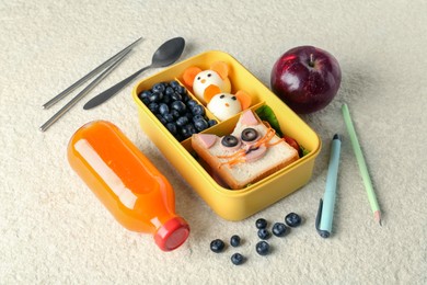 Photo of Lunch box with snacks, bottle of juice, cutlery, pen and pencil on beige textured table