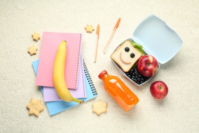 Photo of Lunch box with snacks, bottle of juice and stationery on beige textured table, flat lay