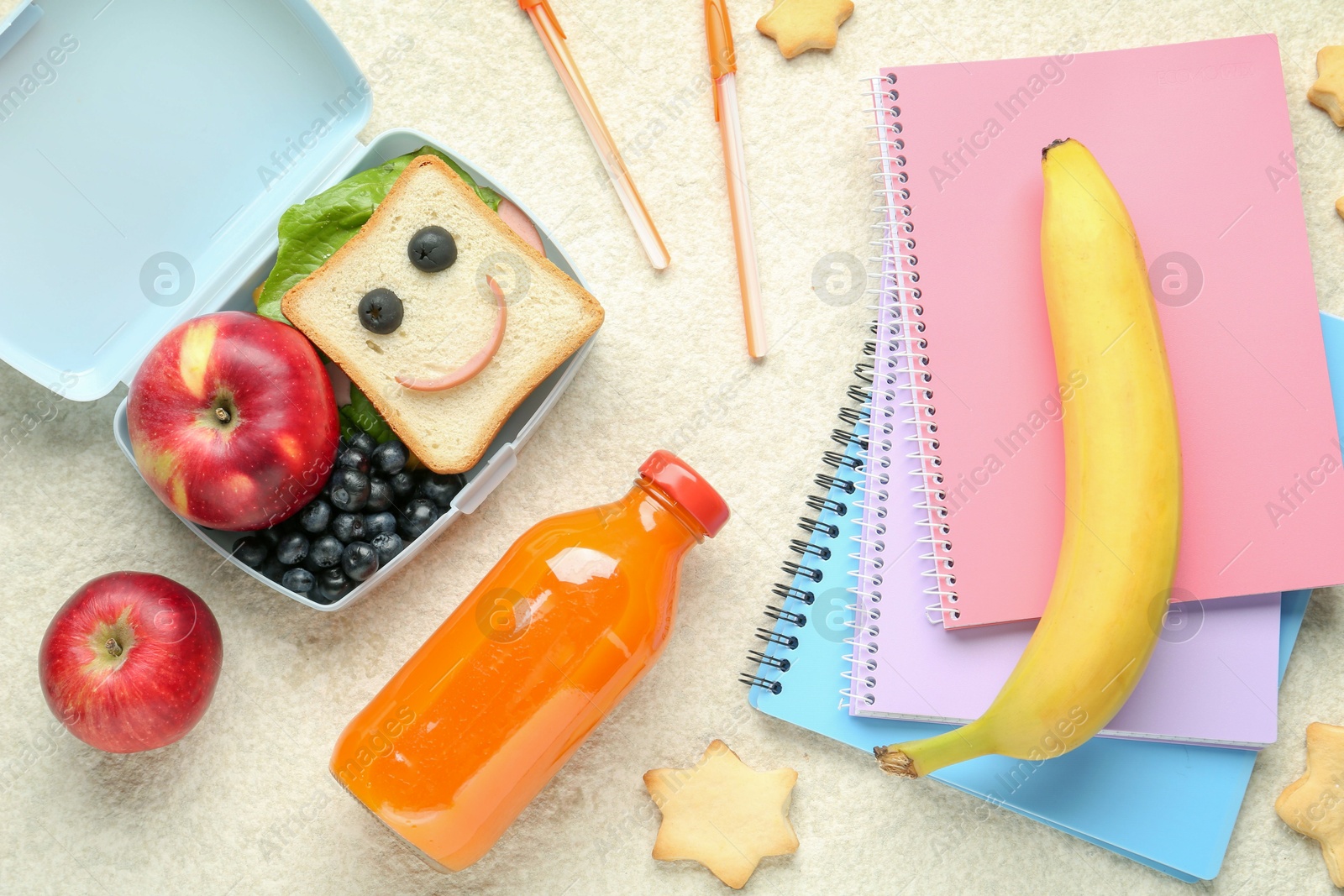 Photo of Lunch box with snacks, bottle of juice and stationery on beige textured table, flat lay