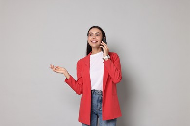 Photo of Beautiful woman in red jacket talking on phone against gray background