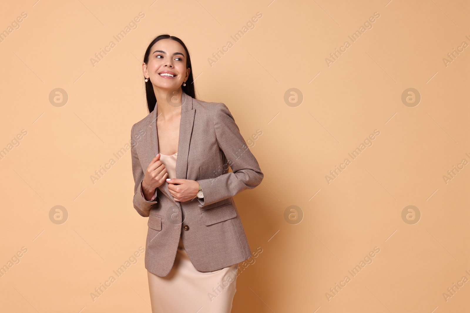 Photo of Beautiful woman in stylish jacket and beige dress on pale orange background, space for text