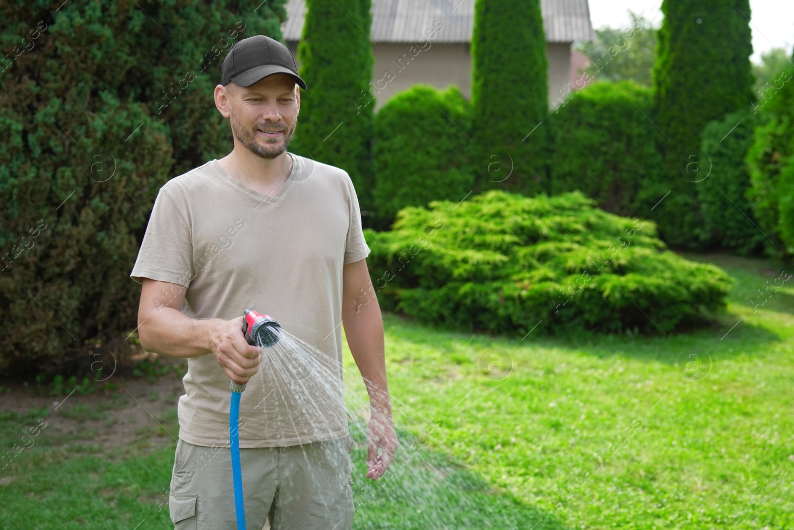 Photo of Man watering lawn with hose in backyard, space for text