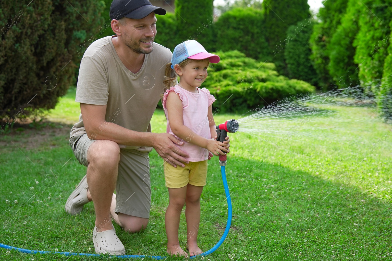 Photo of Father and his daughter watering lawn with hose in backyard