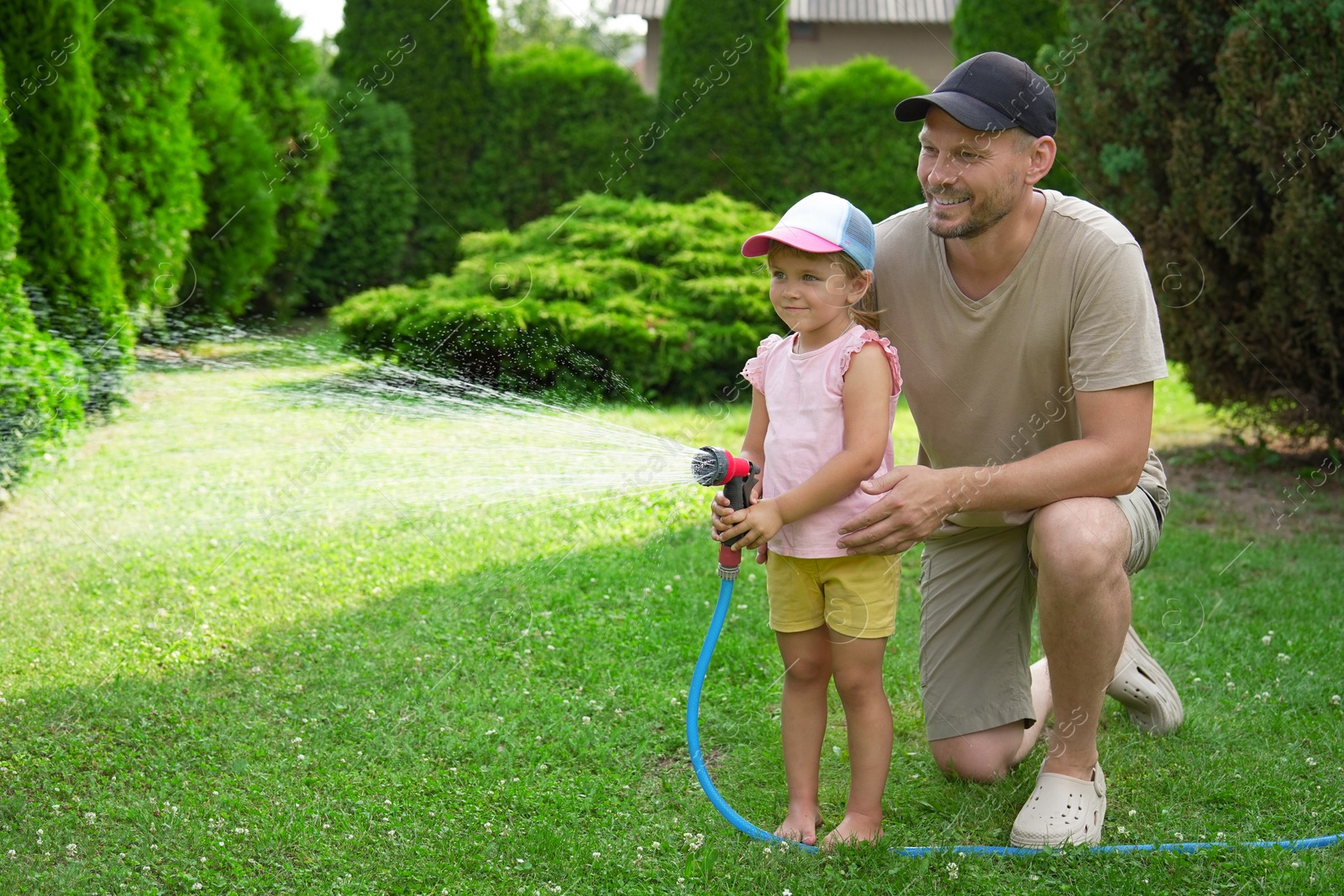 Photo of Father and his daughter watering lawn with hose in backyard