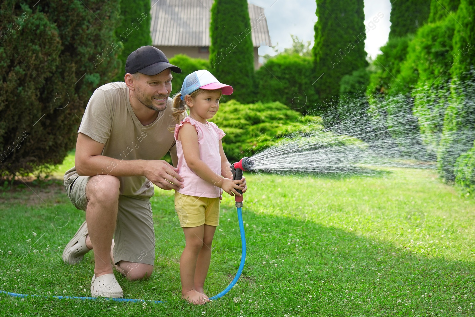 Photo of Father and his daughter watering lawn with hose in backyard