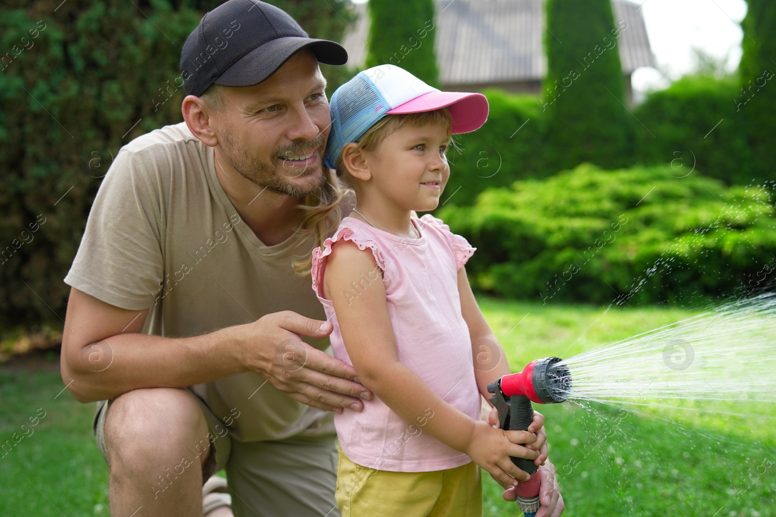 Photo of Father and his daughter watering lawn with hose in backyard