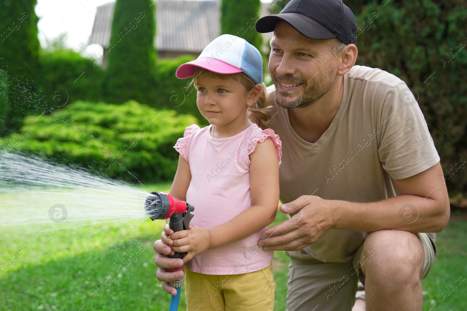 Photo of Father and his daughter watering lawn with hose in backyard