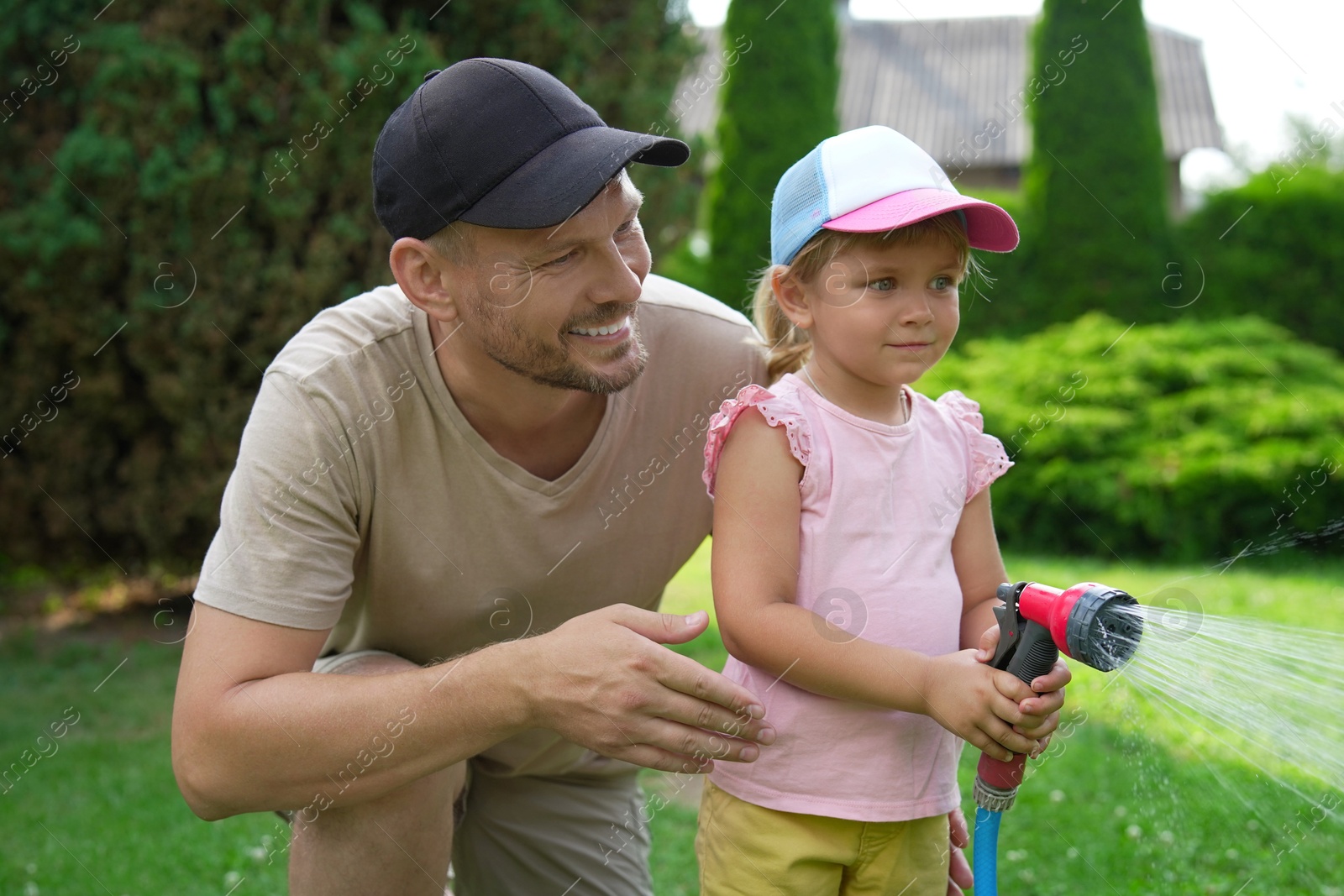 Photo of Father and his daughter watering lawn with hose in backyard