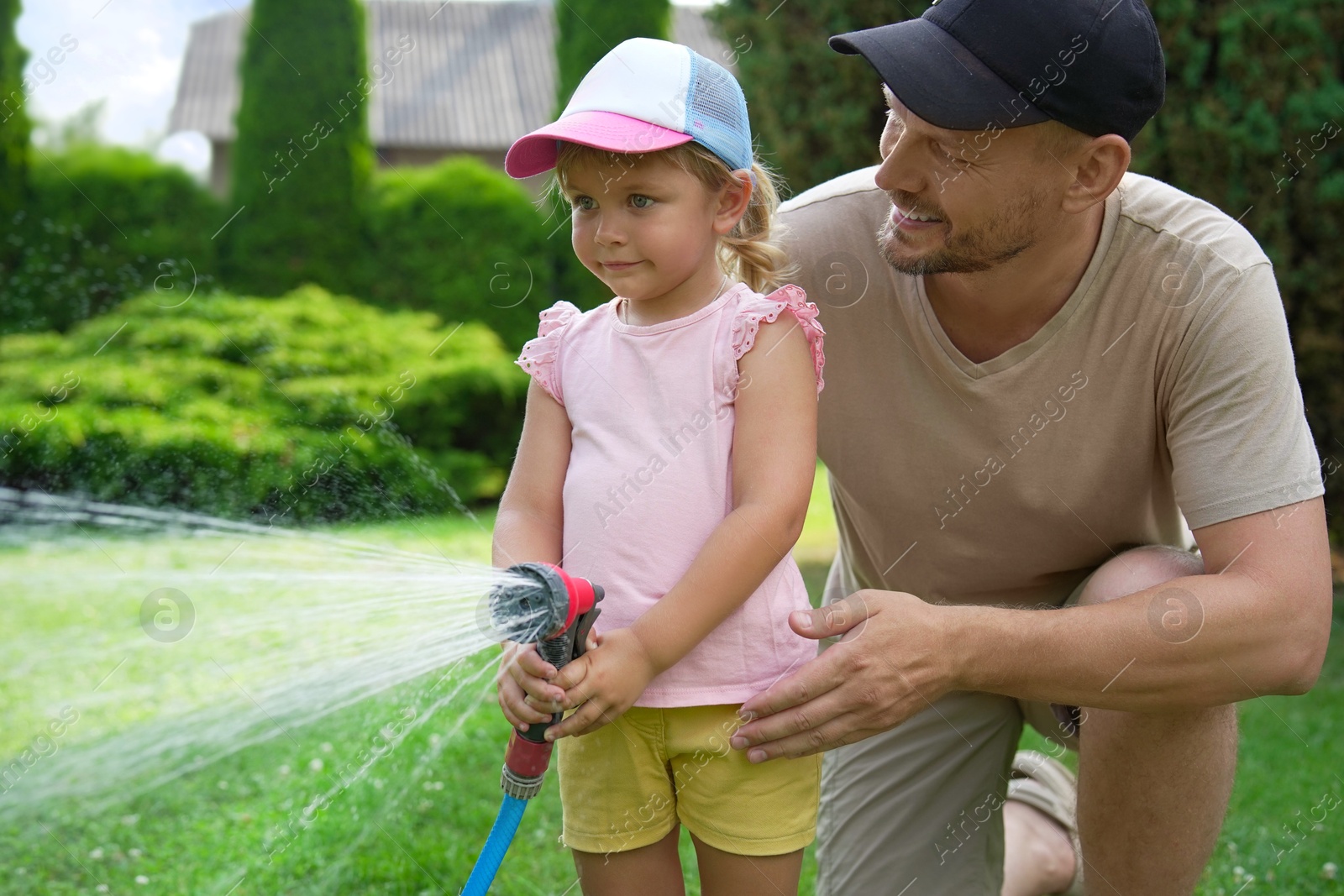 Photo of Father and his daughter watering lawn with hose in backyard