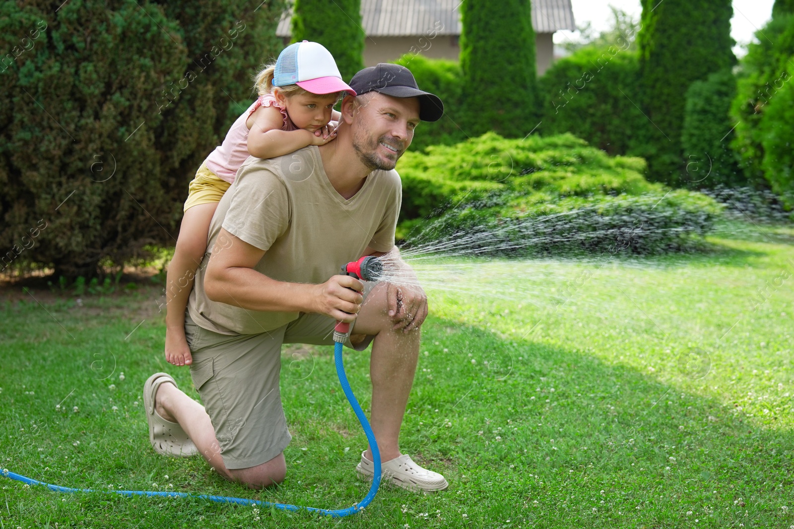 Photo of Father and his daughter watering lawn with hose in backyard