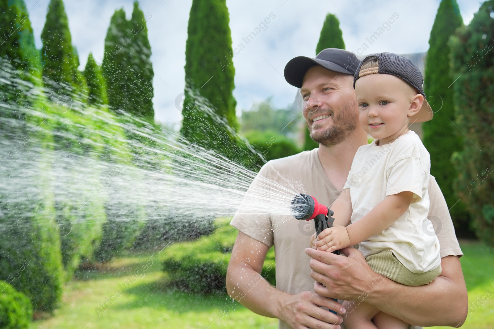 Photo of Father and his son watering lawn with hose in backyard