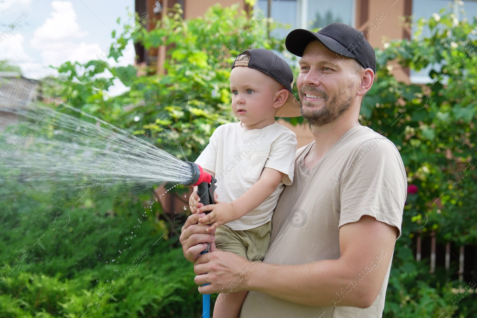 Photo of Father and his son watering lawn with hose in backyard