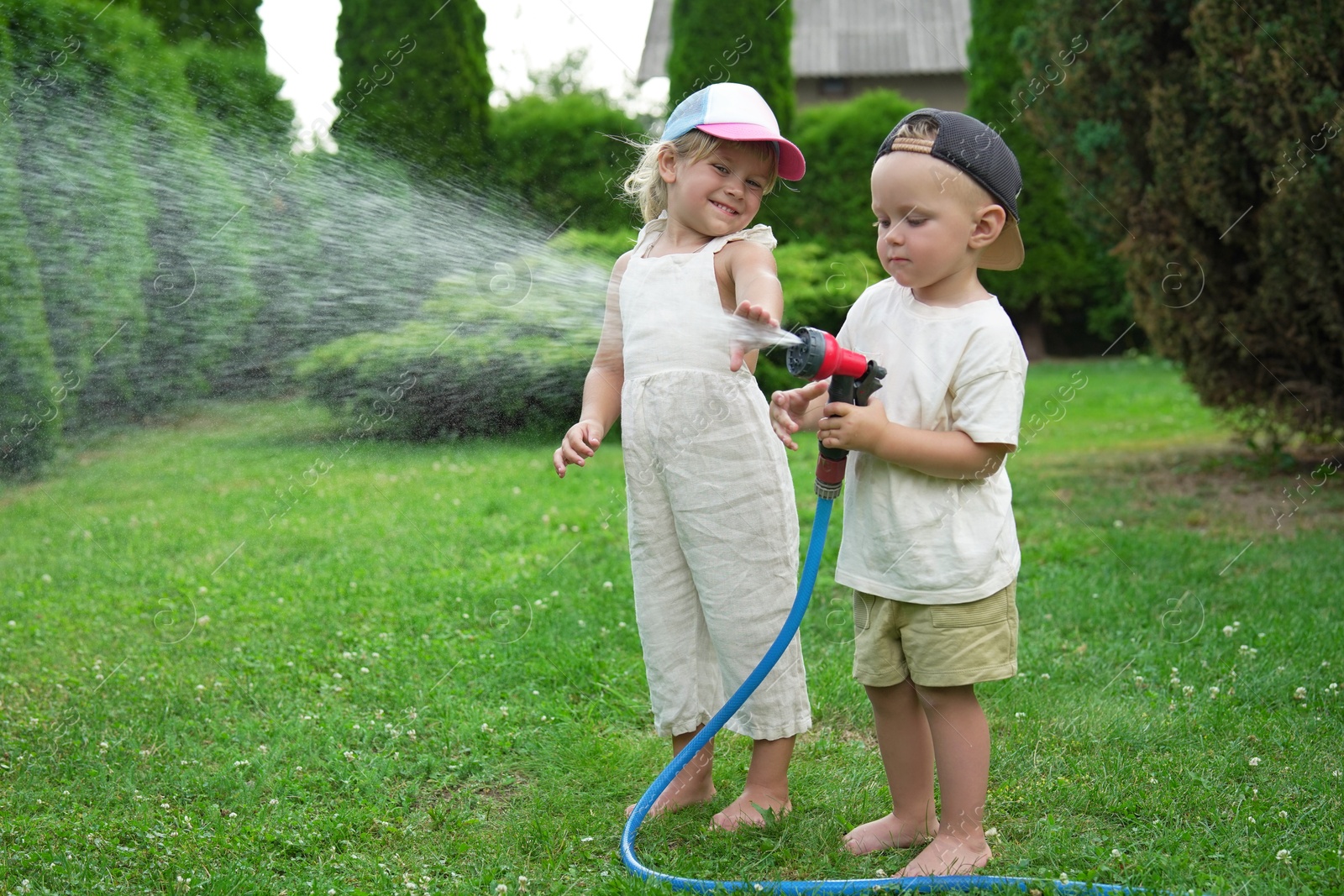 Photo of Little boy and his sister watering lawn with hose in backyard