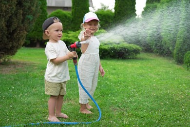 Little boy and his sister watering lawn with hose in backyard