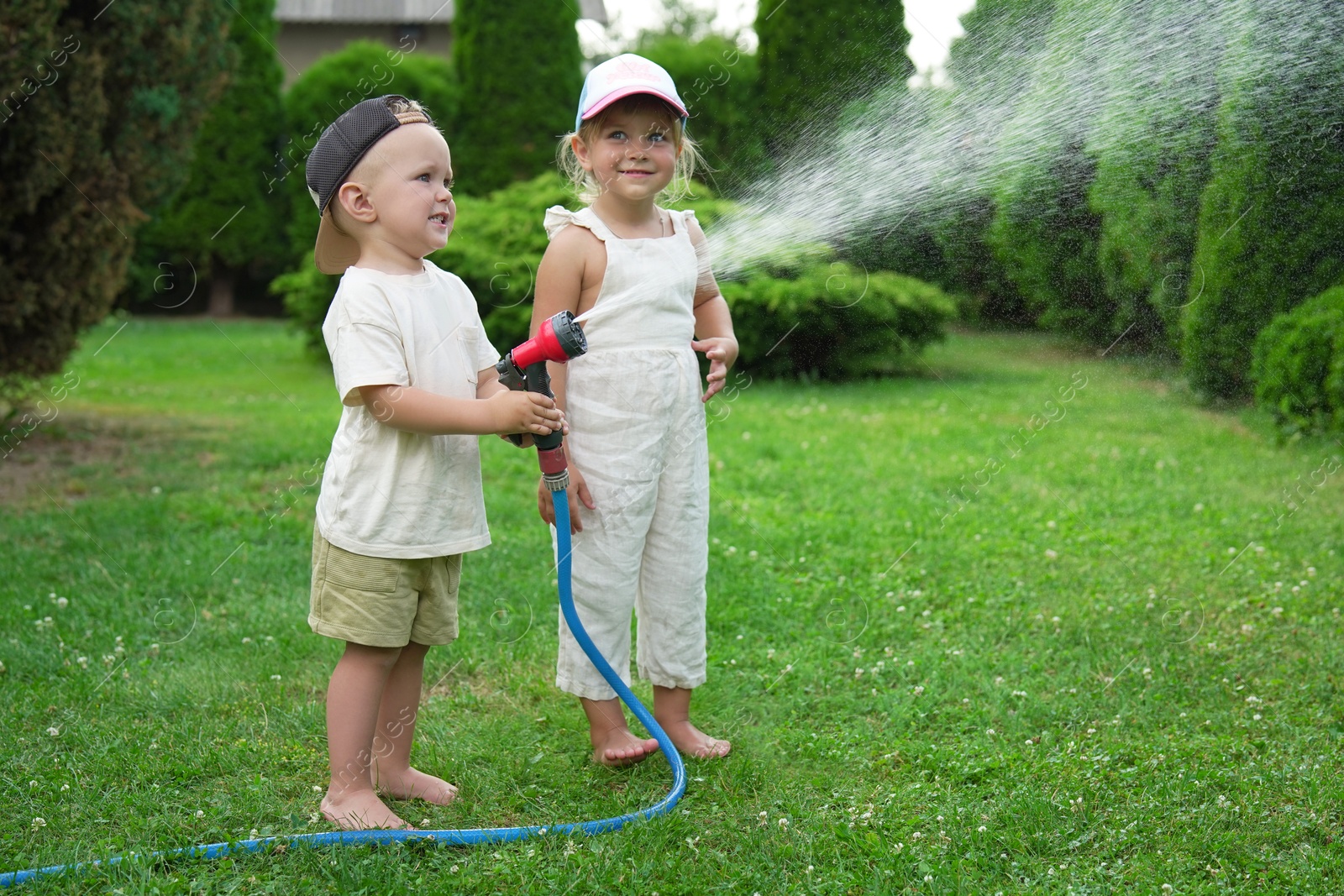 Photo of Little boy and his sister watering lawn with hose in backyard