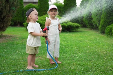 Little boy and his sister watering lawn with hose in backyard