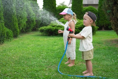 Photo of Little boy and his sister watering lawn with hose in backyard