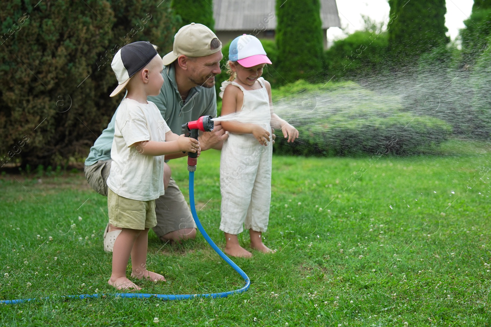 Photo of Father and his kids watering lawn with hose in backyard