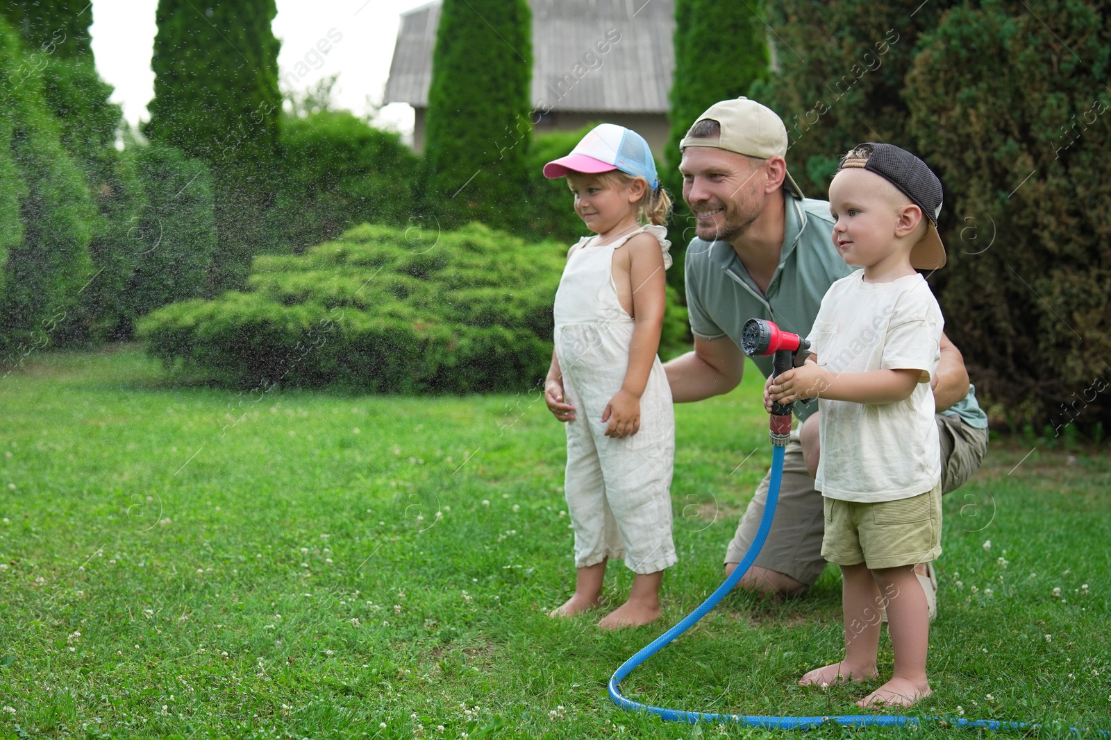 Photo of Father and his kids watering lawn with hose in backyard