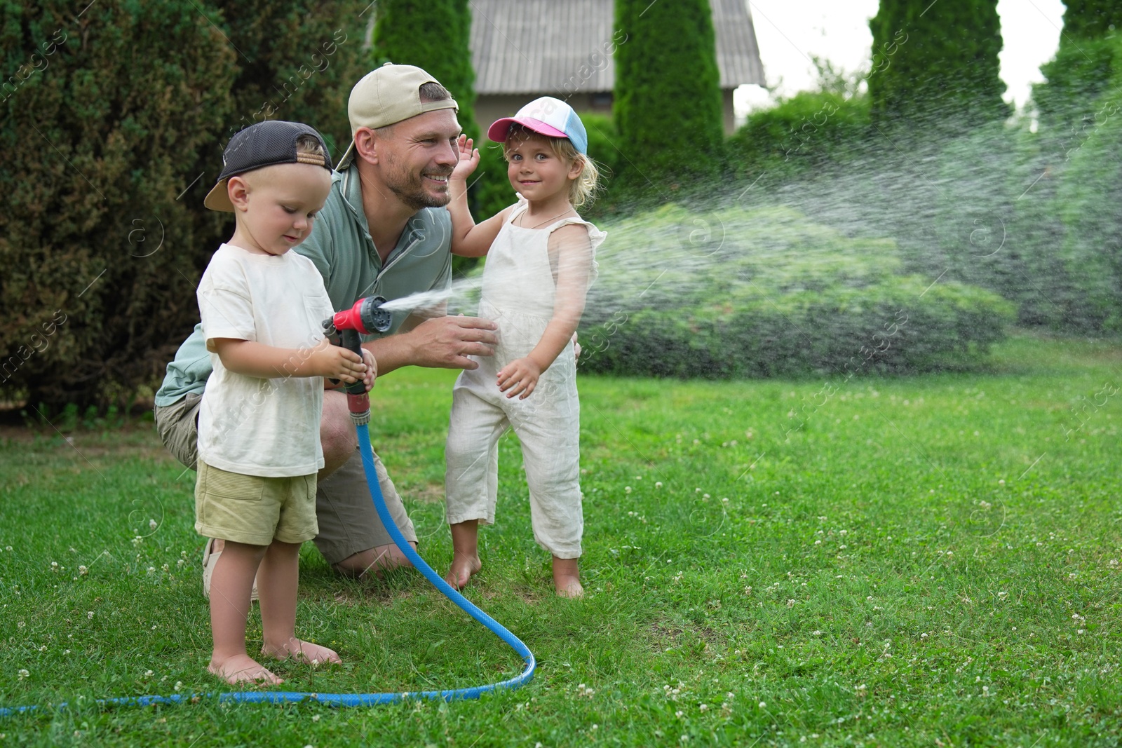 Photo of Father and his kids watering lawn with hose in backyard