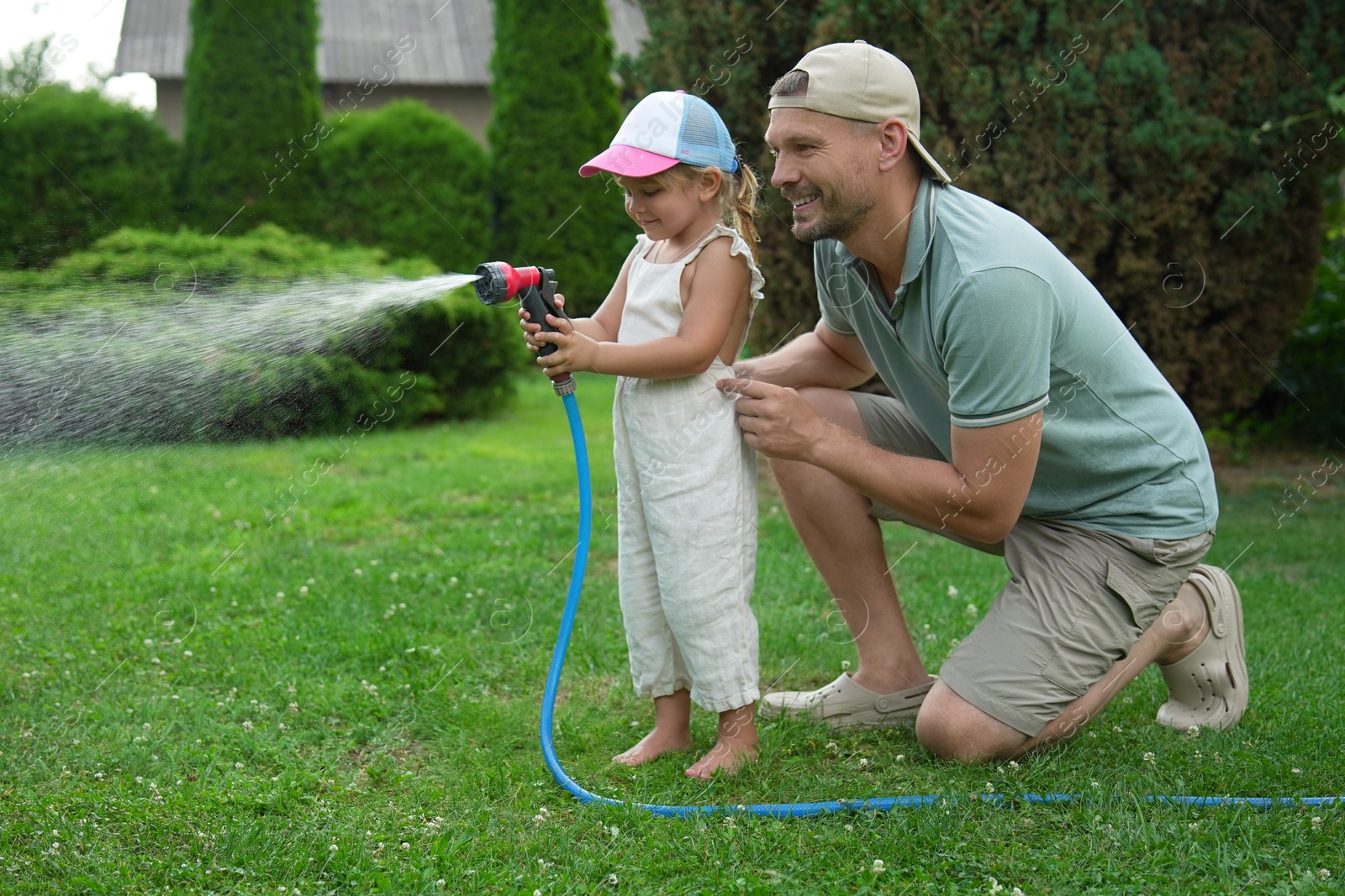 Photo of Father and his daughter watering lawn with hose in backyard