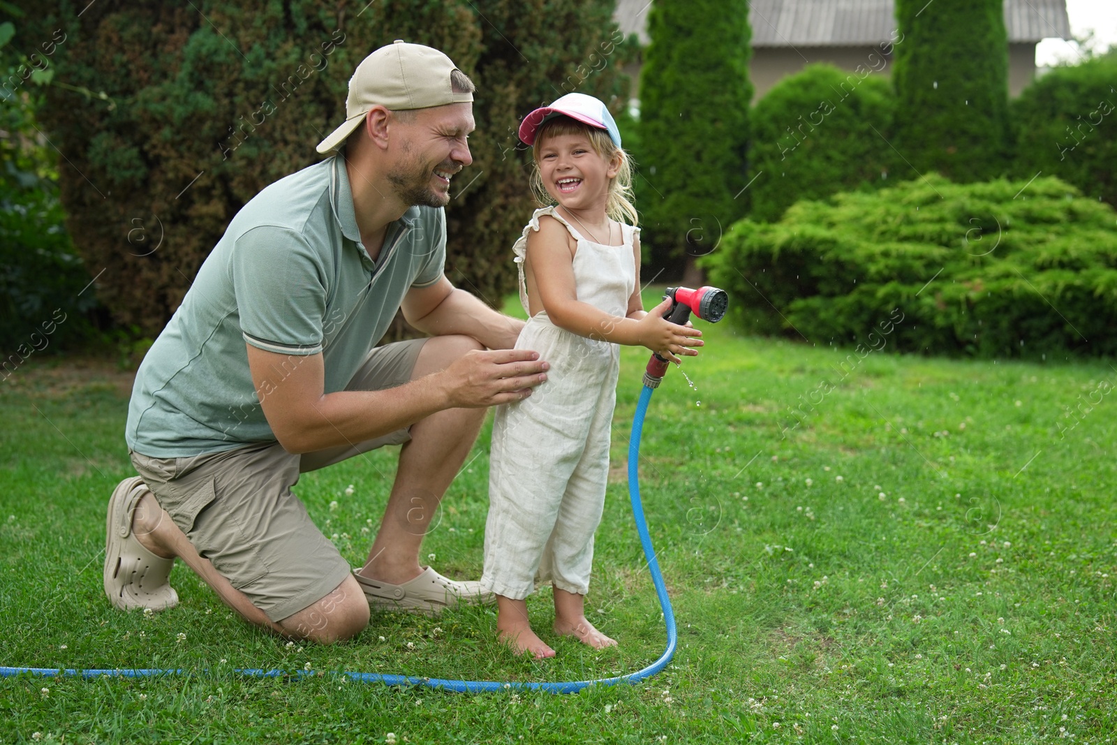 Photo of Father and his daughter watering lawn with hose in backyard, space for text