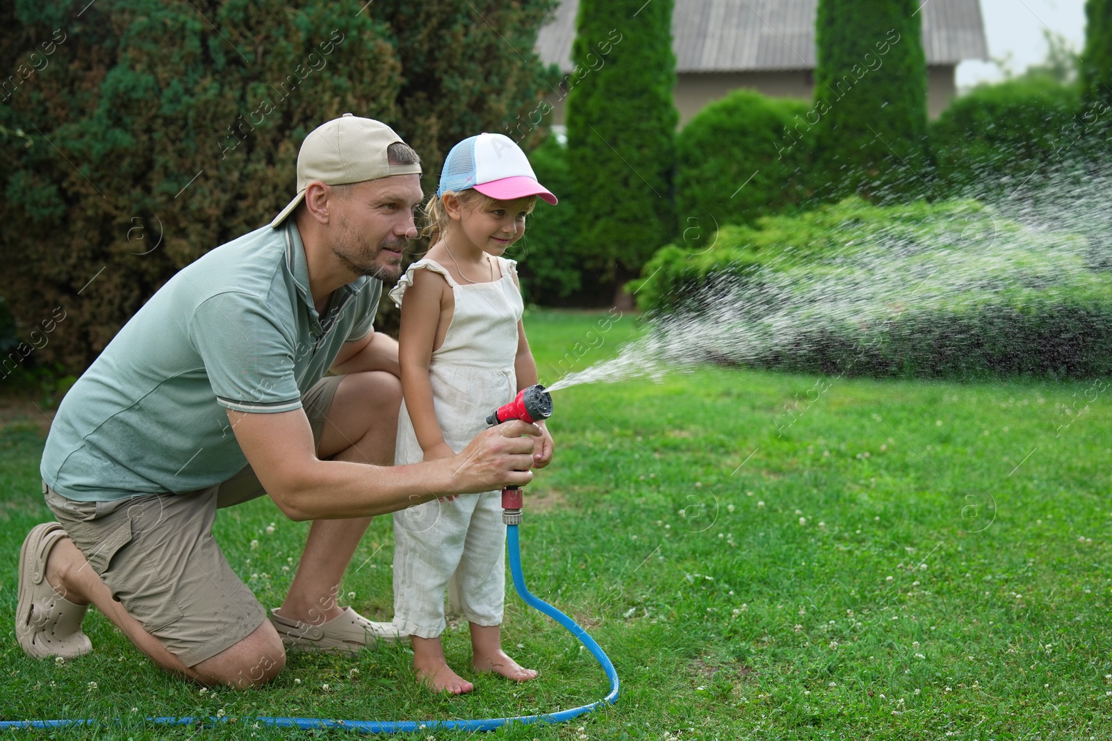 Photo of Father and his daughter watering lawn with hose in backyard