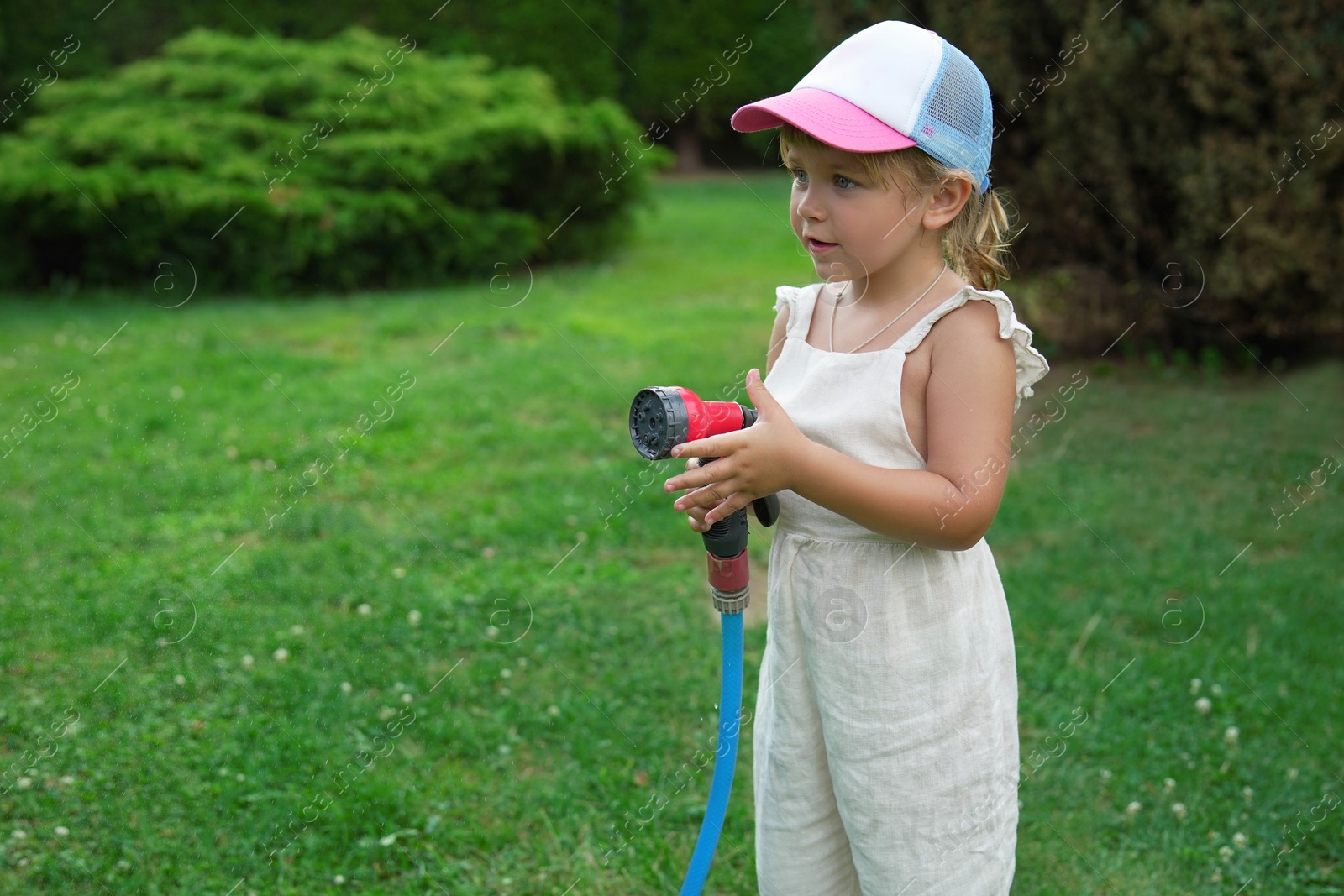 Photo of Little girl watering lawn with hose in backyard, space for text