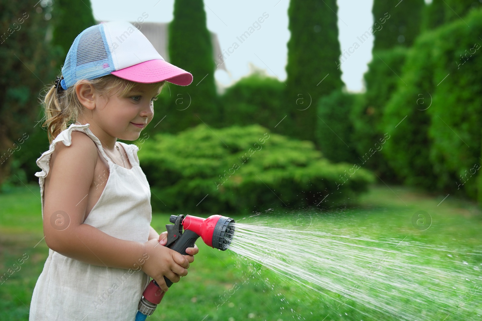 Photo of Little girl watering lawn with hose in backyard