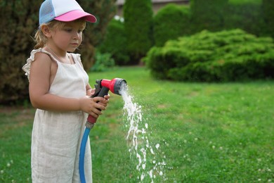 Photo of Little girl watering lawn with hose in backyard, space for text