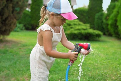 Photo of Little girl watering lawn with hose in backyard