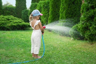 Little girl watering lawn with hose in backyard