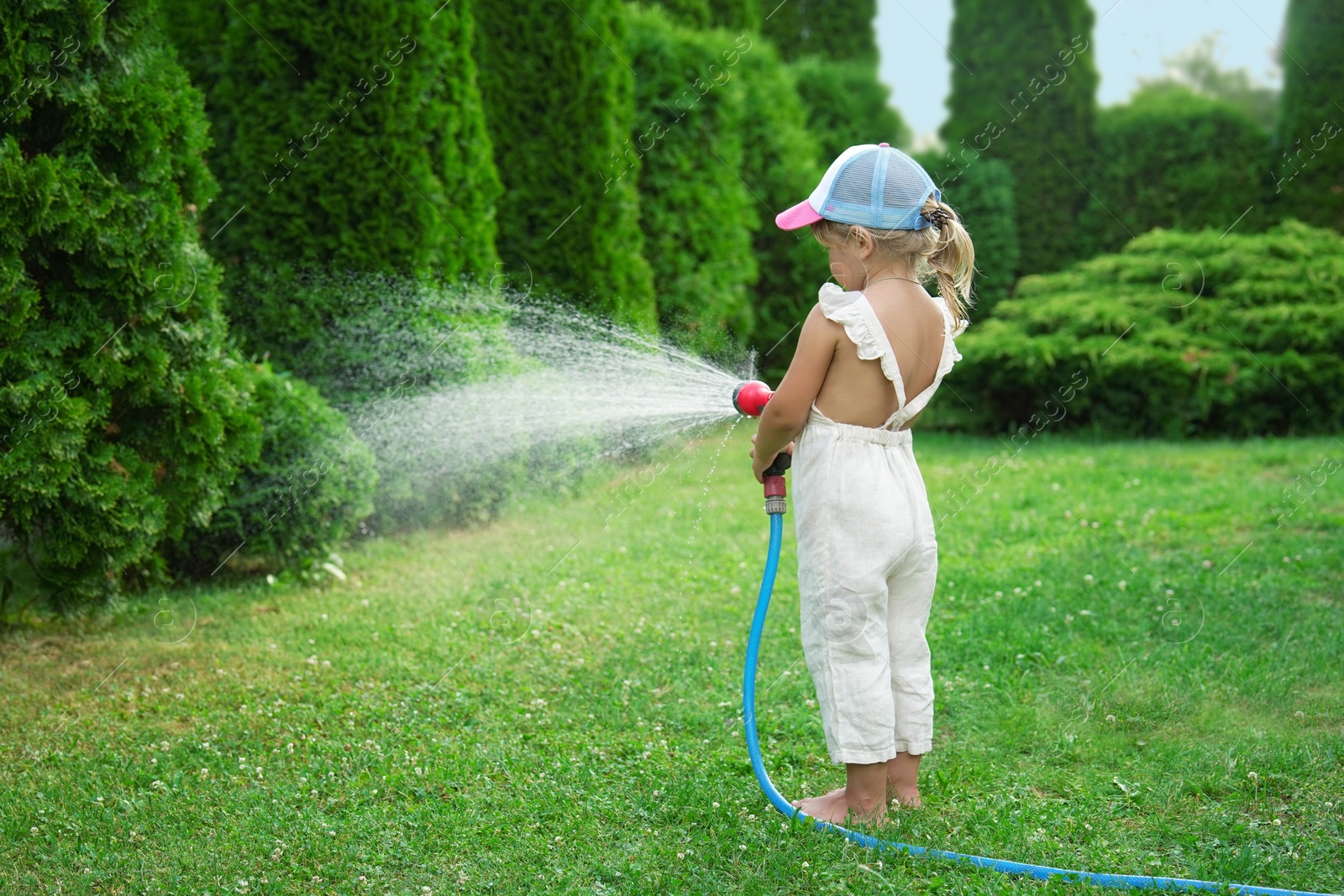 Photo of Little girl watering lawn with hose in backyard