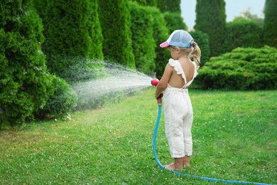 Little girl watering lawn with hose in backyard