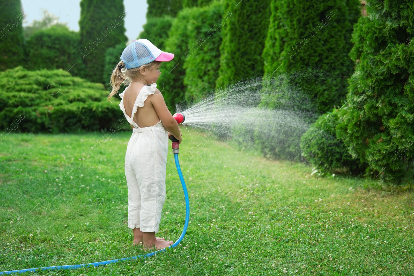 Photo of Little girl watering lawn with hose in backyard