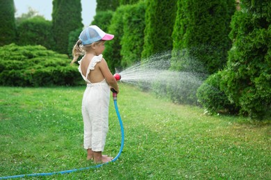 Little girl watering lawn with hose in backyard