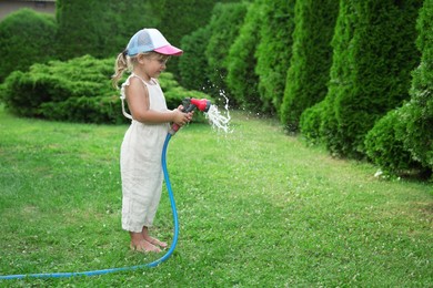 Little girl watering lawn with hose in backyard, space for text