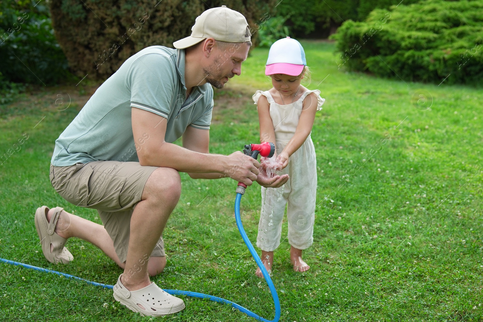 Photo of Father holding hose while his daughter drinking water in backyard