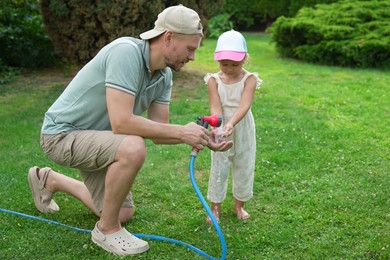 Father holding hose while his daughter drinking water in backyard