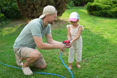 Photo of Father holding hose while his daughter drinking water in backyard