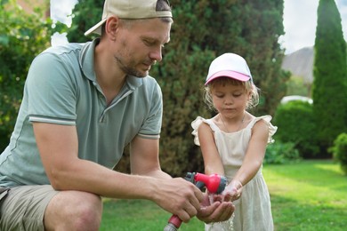 Father holding hose while his daughter drinking water in backyard