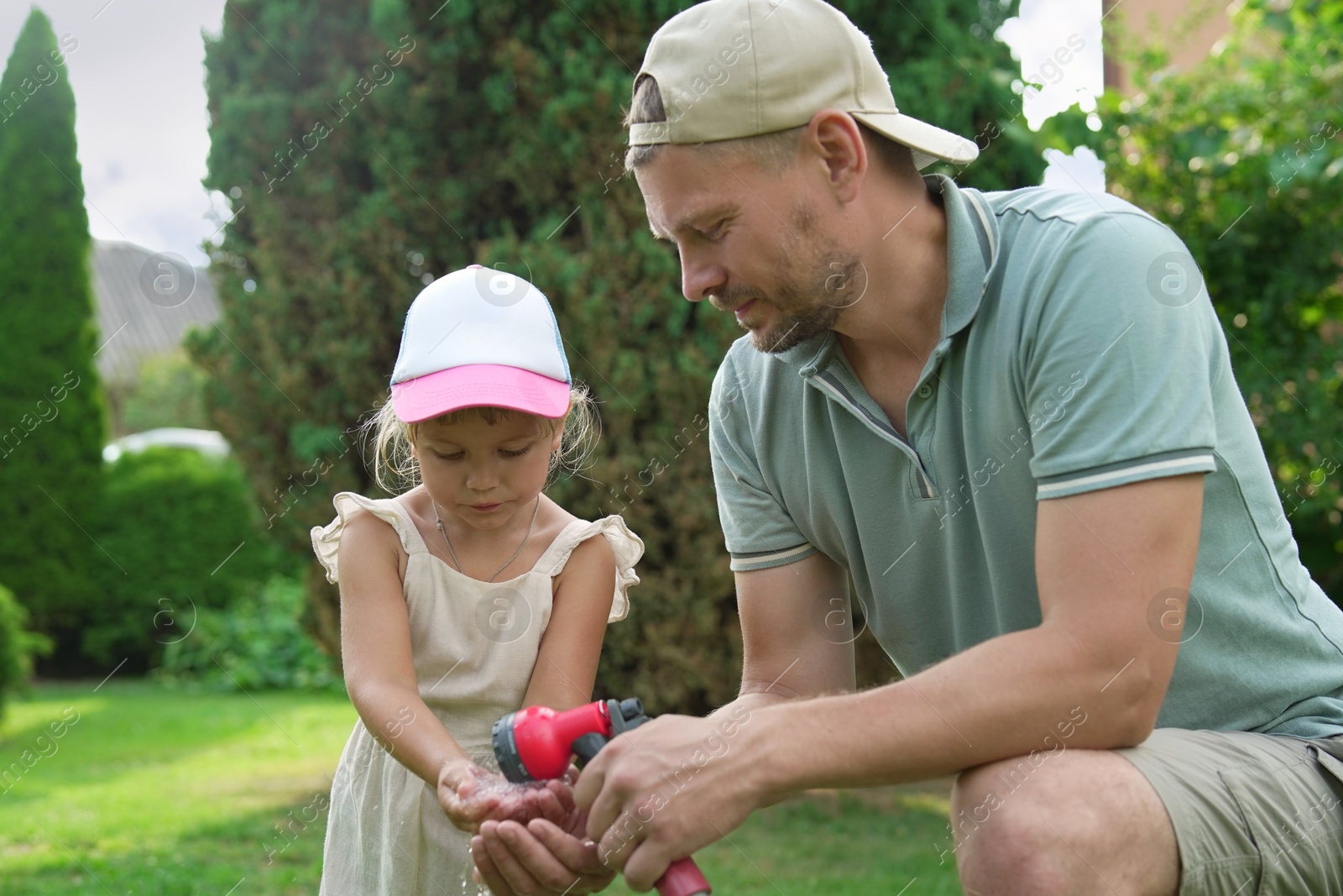 Photo of Father holding hose while his daughter drinking water in backyard