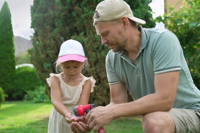 Father holding hose while his daughter drinking water in backyard