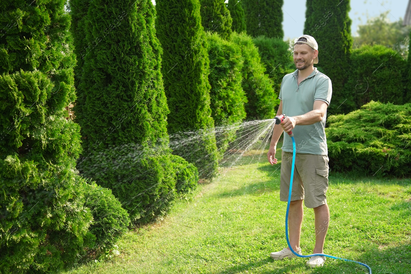 Photo of Man watering lawn with hose in backyard