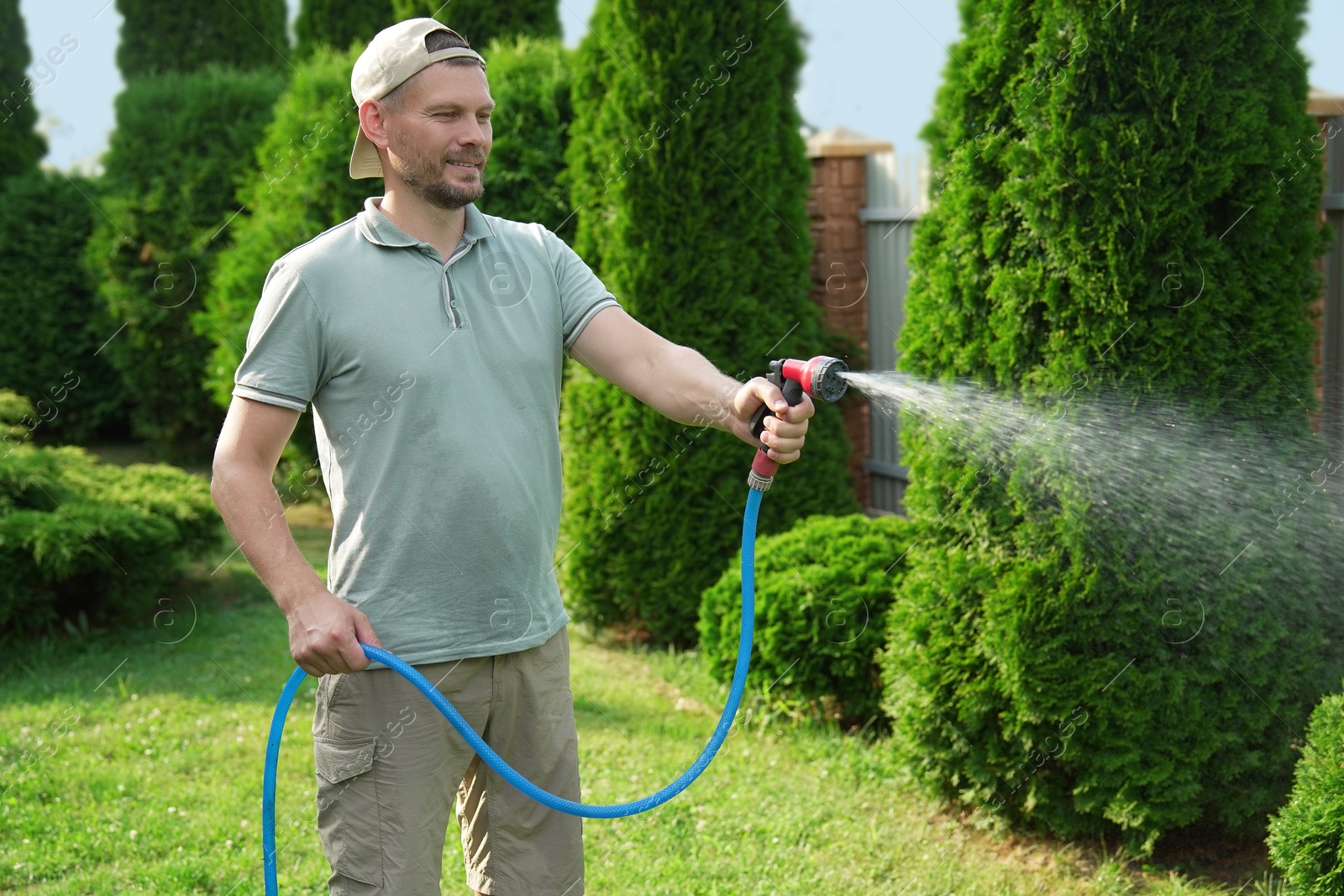 Photo of Man watering lawn with hose in backyard